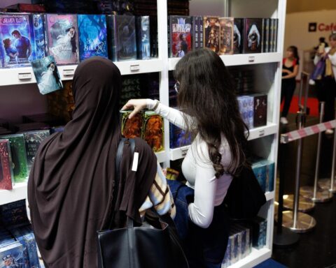 Zwei Frauen betrachten an einem Bücherstand farbig gestaltete Romane.