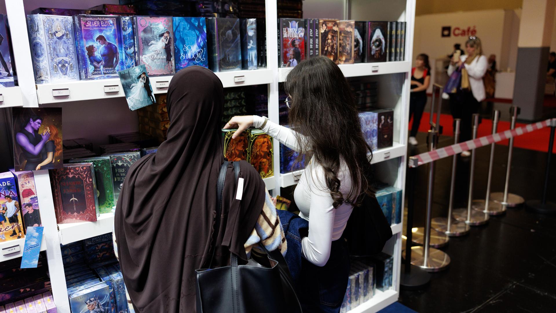 Booktok treibt Verkäufe im deutschen Buchhandel weiter an 1 Zwei Frauen betrachten an einem Bücherstand farbig gestaltete Romane.
