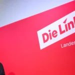 Eine Frau spricht an einem Podium vor einer roten Wand mit dem Schriftzug „Die Linke Landesverband Berlin“.