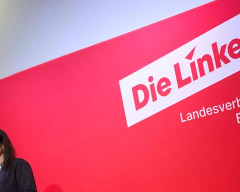 Eine Frau spricht an einem Podium vor einer roten Wand mit dem Schriftzug „Die Linke Landesverband Berlin“.