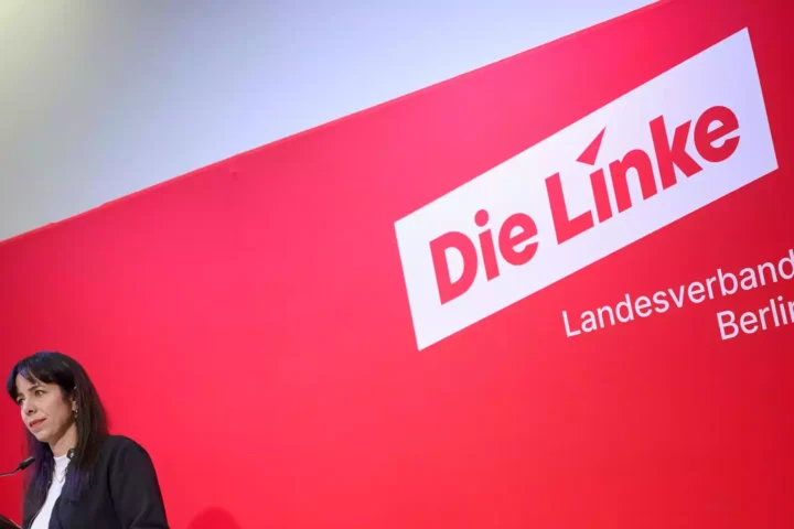 Eine Frau spricht an einem Podium vor einer roten Wand mit dem Schriftzug „Die Linke Landesverband Berlin“.