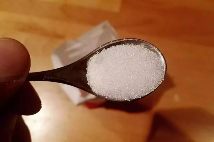 Nahaufnahme eines Löffels mit weißem Zucker in einer Hand.