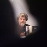 Reinhold Messner sitzt bei einer Veranstaltung und hält ein Mikrofon.