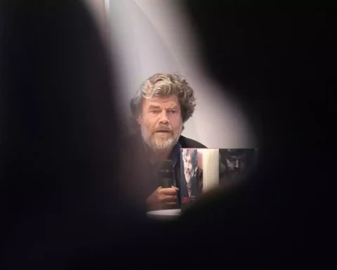 Reinhold Messner sitzt bei einer Veranstaltung und hält ein Mikrofon.