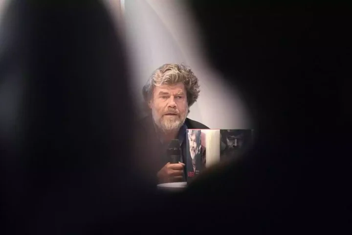 Reinhold Messner sitzt bei einer Veranstaltung und hält ein Mikrofon.