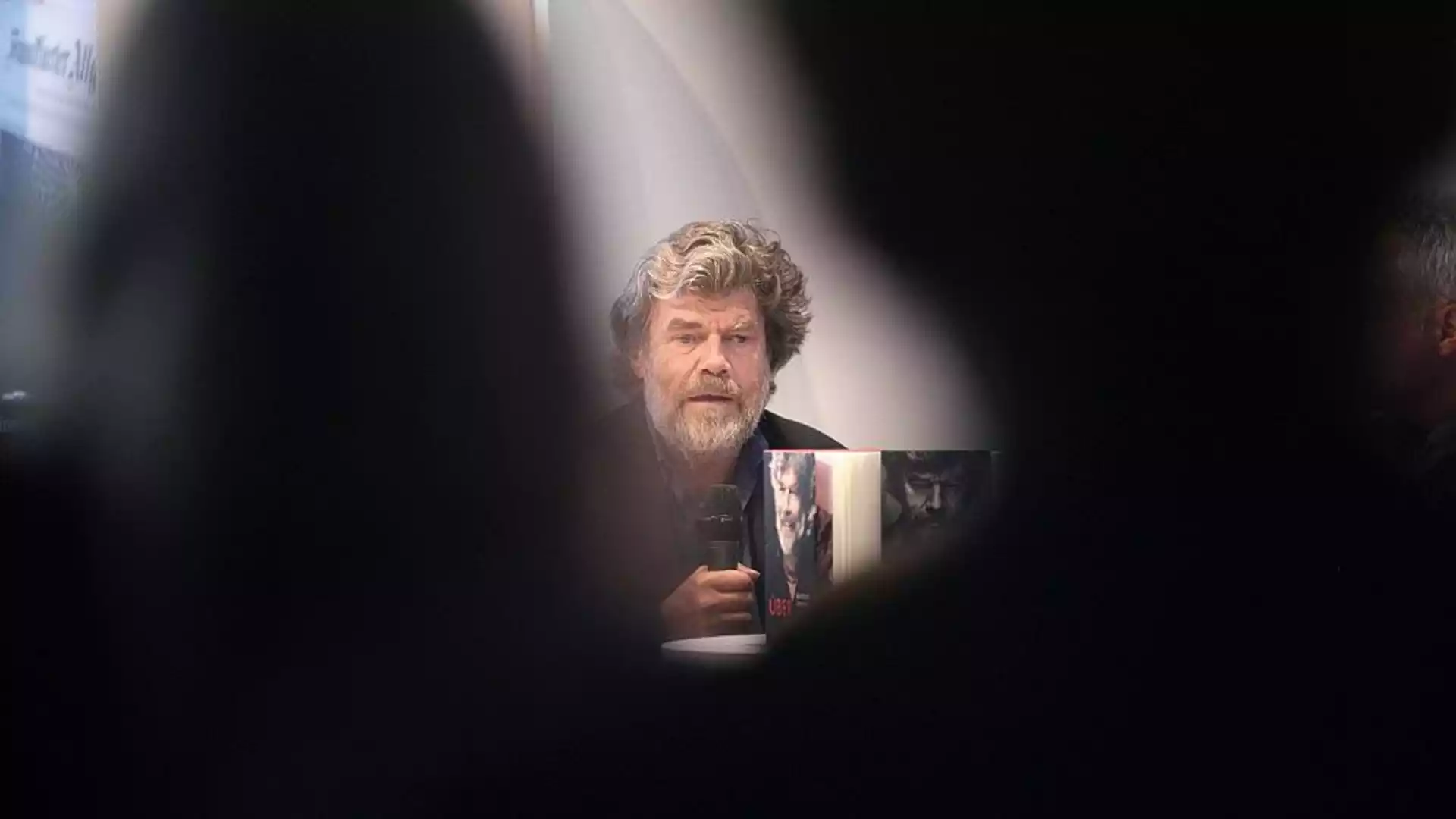 Reinhold Messner sitzt bei einer Veranstaltung und hält ein Mikrofon.