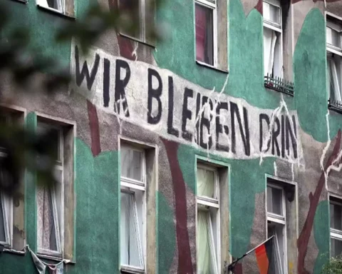 Wohnhausfassade mit großem Protestschriftzug „Wir bleiben drin“.