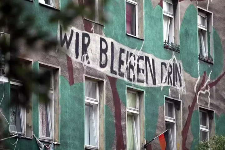 Wohnhausfassade mit großem Protestschriftzug „Wir bleiben drin“.