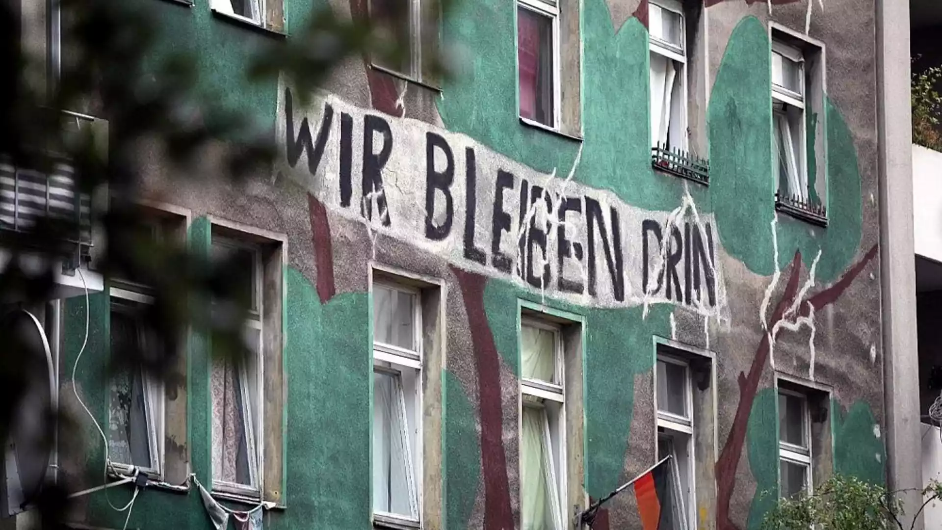 Wohnhausfassade mit großem Protestschriftzug „Wir bleiben drin“.