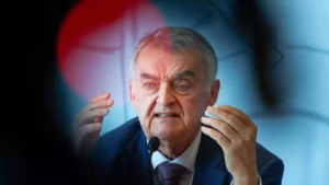 Herbert Reul spricht an einem Mikrofon und gestikuliert mit beiden Händen.