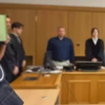Nahaufnahme einer Justiz-Uniform mit Abzeichen vor einer Gerichtsszene im Hintergrund.