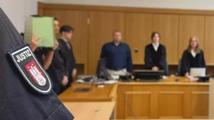 Nahaufnahme einer Justiz-Uniform mit Abzeichen vor einer Gerichtsszene im Hintergrund.