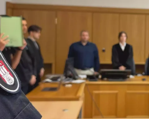 Nahaufnahme einer Justiz-Uniform mit Abzeichen vor einer Gerichtsszene im Hintergrund.