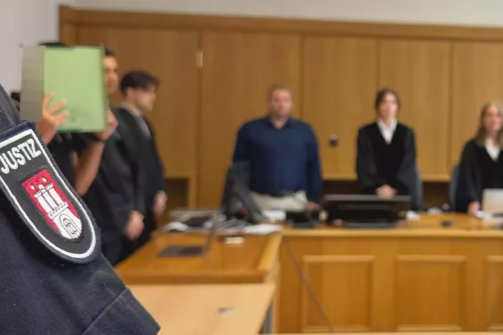 Nahaufnahme einer Justiz-Uniform mit Abzeichen vor einer Gerichtsszene im Hintergrund.