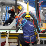 Mitarbeiter mit Schutzhelmen arbeiten in einer Fertigungshalle an einem großen Bauteil mit Nordex-Aufdruck.