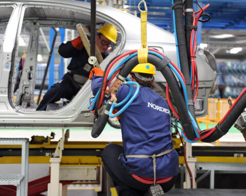 Mitarbeiter mit Schutzhelmen arbeiten in einer Fertigungshalle an einem großen Bauteil mit Nordex-Aufdruck.