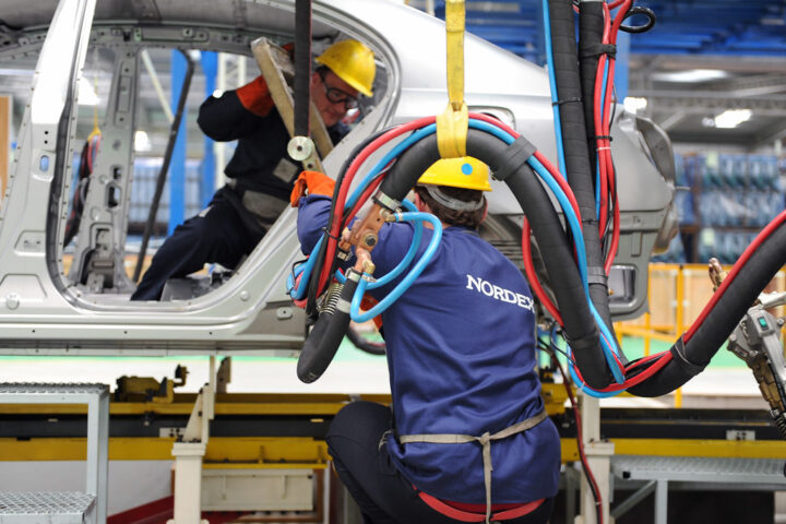Mitarbeiter mit Schutzhelmen arbeiten in einer Fertigungshalle an einem großen Bauteil mit Nordex-Aufdruck.