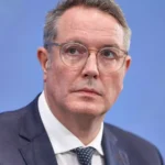 Alexander Schweitzer im Anzug vor blauem Hintergrund.