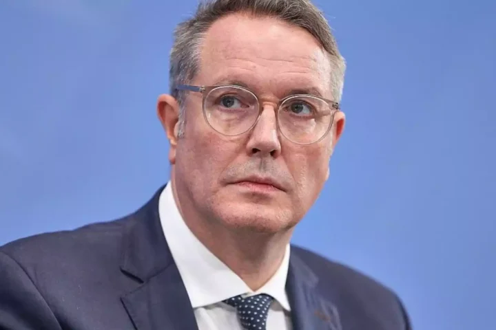 Alexander Schweitzer im Anzug vor blauem Hintergrund.