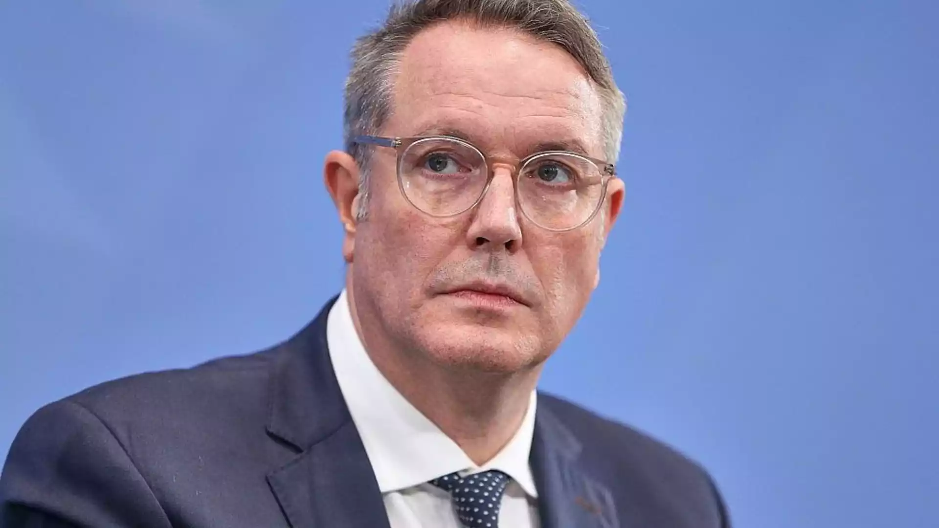 Alexander Schweitzer im Anzug vor blauem Hintergrund.