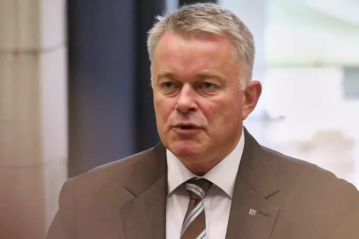Mann im Anzug spricht in Innenraum, porträtiert vor unscharfem Hintergrund.