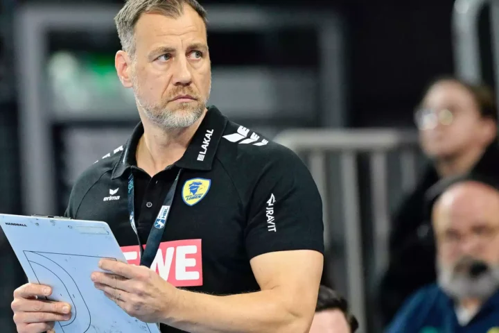 Maik Machulla steht mit Klemmbrett am Spielfeldrand in schwarzem Rhein-Neckar-Löwen-Poloshirt.
