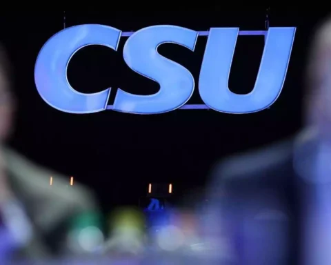 CSU-Logo vor dunklem Hintergrund, unscharfe Personen im Vordergrund.