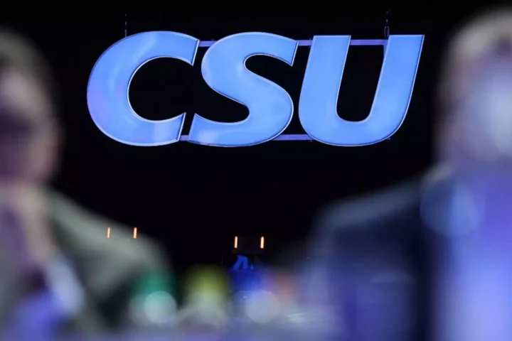 CSU-Logo vor dunklem Hintergrund, unscharfe Personen im Vordergrund.