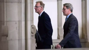 Andreas Scheuer geht in dunklem Anzug durch einen Innenraum mit Säulen.