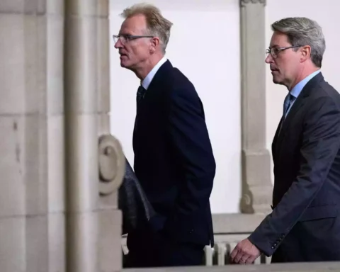 Andreas Scheuer geht in dunklem Anzug durch einen Innenraum mit Säulen.