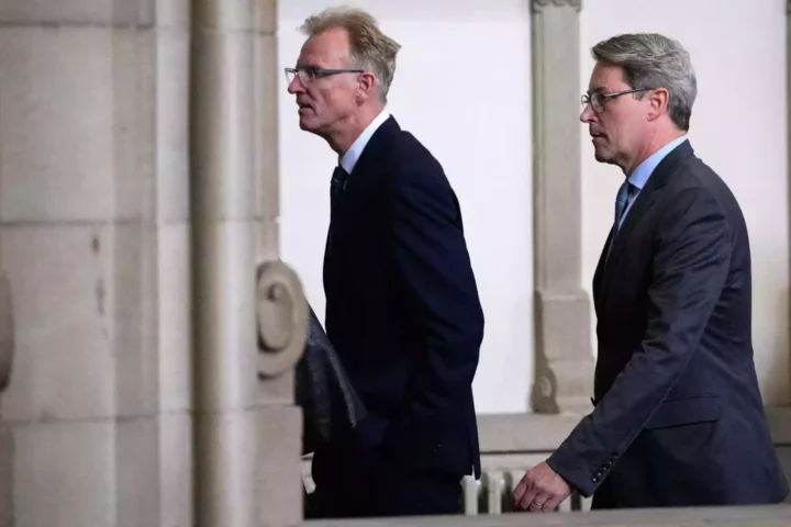 Andreas Scheuer geht in dunklem Anzug durch einen Innenraum mit Säulen.
