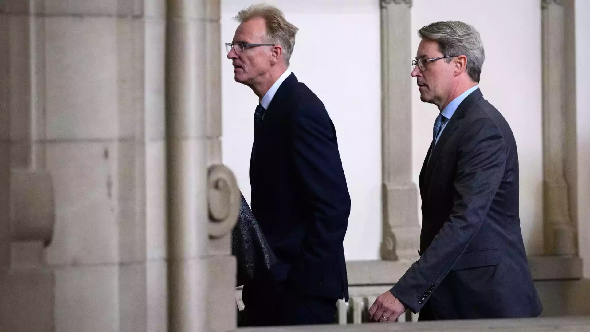 Andreas Scheuer geht in dunklem Anzug durch einen Innenraum mit Säulen.