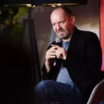 Philippe Sands sitzt mit einem Mikrofon auf einer Bühne bei einer Veranstaltung.