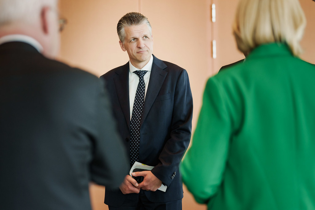 Friedrich Merz steht in einem Raum und spricht mit zwei Personen im Vordergrund.