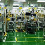Blick in eine automatisierte Produktionshalle mit Robotern, Maschinen und grünen Bodenmarkierungen.