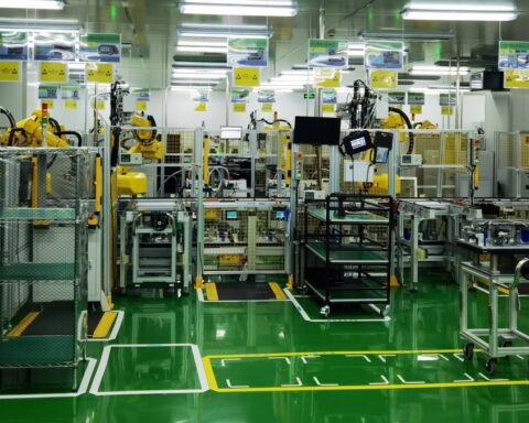 Blick in eine automatisierte Produktionshalle mit Robotern, Maschinen und grünen Bodenmarkierungen.
