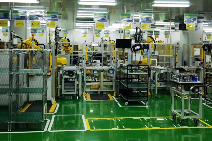 Blick in eine automatisierte Produktionshalle mit Robotern, Maschinen und grünen Bodenmarkierungen.