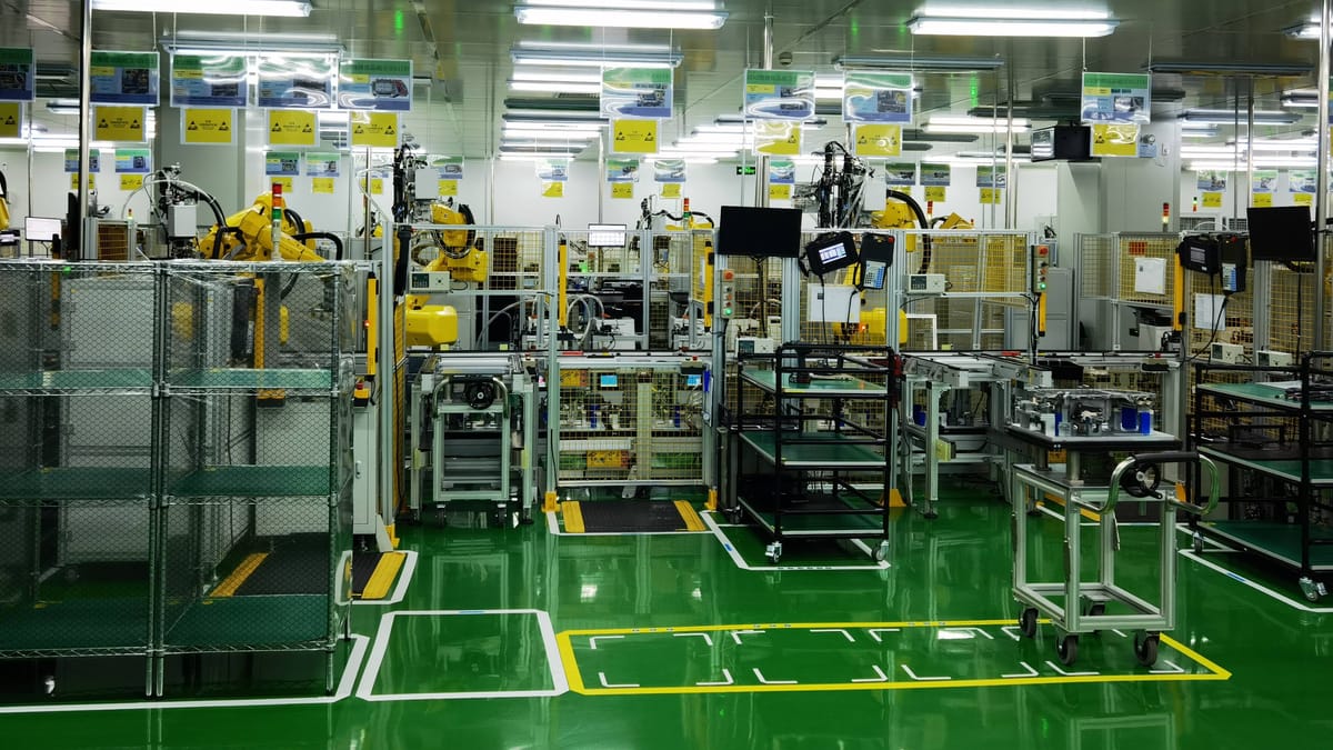 Blick in eine automatisierte Produktionshalle mit Robotern, Maschinen und grünen Bodenmarkierungen.