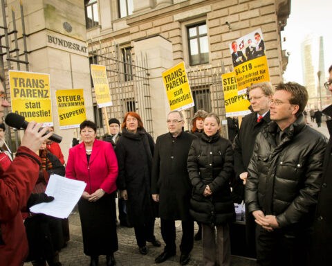 Menschen stehen vor dem Bundesrat in Berlin bei einer Protest- oder Kundgebungsaktion mit gelben Transparenten.