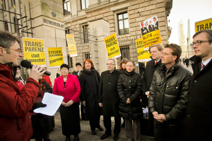 Menschen stehen vor dem Bundesrat in Berlin bei einer Protest- oder Kundgebungsaktion mit gelben Transparenten.
