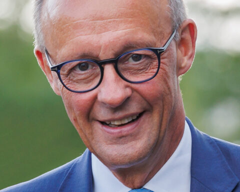 Friedrich Merz lächelt in blauem Anzug und mit Brille in einer Porträtaufnahme.