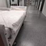 Ein Bett mit Schutzfolie steht in einem Krankenhausflur.