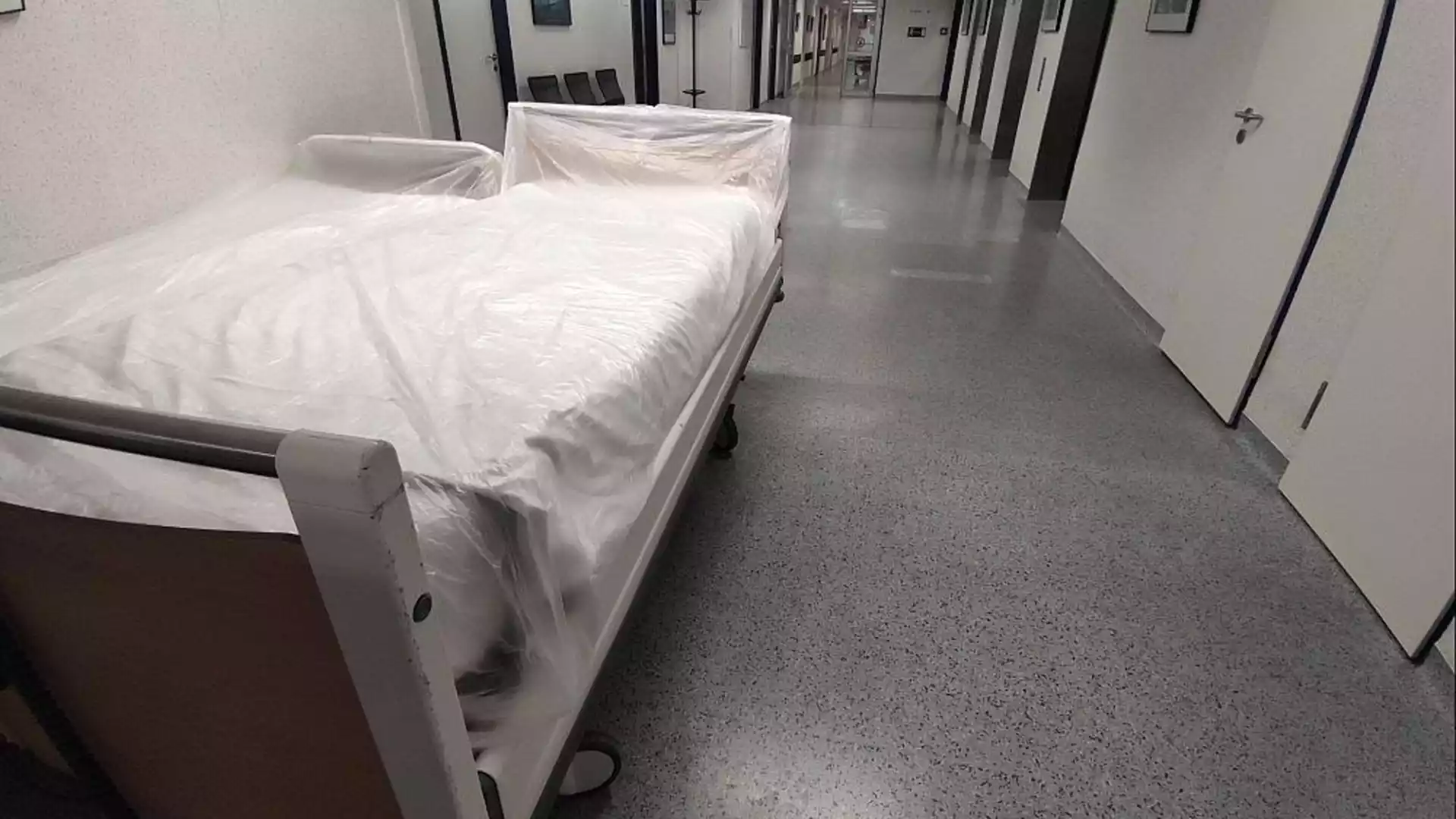 Ein Bett mit Schutzfolie steht in einem Krankenhausflur.