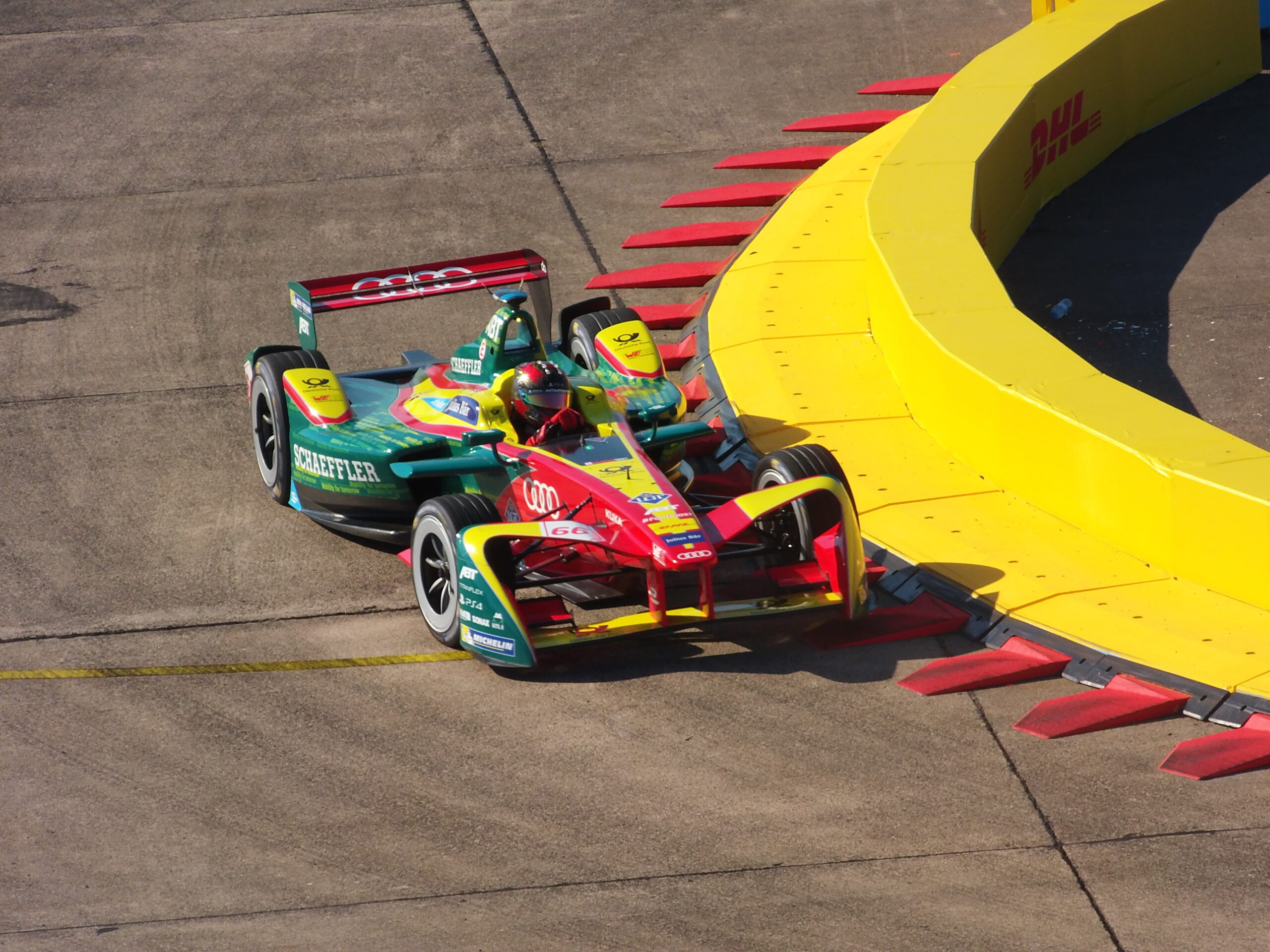 Formel-E-Rennwagen mit Schaeffler-Branding fährt auf einer Rennstrecke an einer gelben Barriere vorbei.