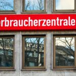 Rotes Schild mit der Aufschrift „verbraucherzentrale“ an einer Gebäudefassade.