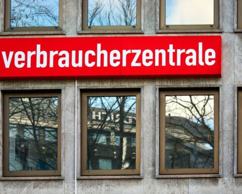 Rotes Schild mit der Aufschrift „verbraucherzentrale“ an einer Gebäudefassade.