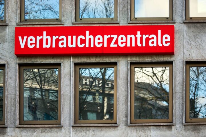 Rotes Schild mit der Aufschrift „verbraucherzentrale“ an einer Gebäudefassade.
