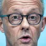 Nahaufnahme von Friedrich Merz mit Brille vor blauem Hintergrund