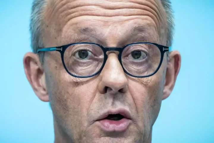 Nahaufnahme von Friedrich Merz mit Brille vor blauem Hintergrund