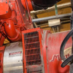Rote industrielle Generator- oder Motoranlage mit Warnschild und Kabeln in einer Maschinenumgebung.